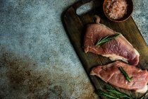 Vue de dessus des steaks de porc cru au romarin et au sel d'himalaya rose — Photo de stock