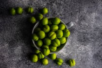 Mug of green plums on concrete surface, top view — Stock Photo