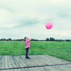 Menina sorridente de pé em um prado segurando um balão rosa, Polônia — Fotografia de Stock