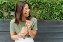 Portrait of a woman with holding a paloma cocktail sitting on a bench laughing — Stock Photo