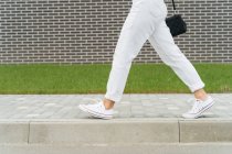 Pernas de mulher em calças brancas passando por uma parede de tijolo — Fotografia de Stock