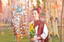 Portrait d'une femme souriante en vêtements traditionnels thaïlandais tenant des fleurs, Thaïlande — Photo de stock