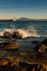 Ondas Bater na praia de Playa Chica com estátua do Sagrado Coração de Jesus e Punta del Santo à distância, Tarifa, Cádiz, Andaluzia, Espanha — Fotografia de Stock
