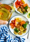 Two servings of grilled salmon steak with roasted courgettes, tomatoes, lemon and hand holding glass of white wine — Stock Photo