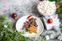 Рождественский подарок рядом с тарелкой пряничных человечков печенье и чашка мини зефира — стоковое фото