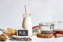 Cuenco de cereal junto a una botella de leche, semillas de chía y miel con una pizarra - foto de stock