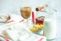 Чашка хлопьев, молоко, мед и чашка кофе на столе рядом с чайным полотенцем — стоковое фото