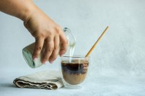 Frau gießt Milch in eine Tasse Kaffee — Stockfoto