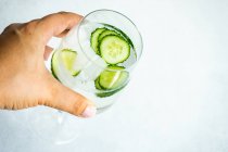 Woman's hand holding a glass of water with ice cubes and cucumber — Stock Photo