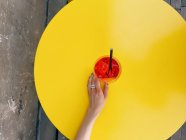 Overhead view of a woman reaching for an aperol spritz cocktail on yellow table — Stock Photo