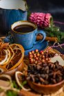 Weihnachtlicher Gewürzkaffee in blauer Keramiktasse zwischen Gewürzen und Beeren auf dunklem launischen Hintergrund — Stockfoto