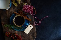 Café com especiarias de Natal em caneca de cerâmica azul entre especiarias e bagas em fundo escuro e mal-humorado — Fotografia de Stock