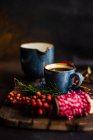 Caffè speziato natalizio in tazza di ceramica blu tra spezie e bacche su sfondo scuro lunatico — Foto stock