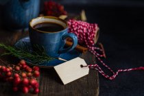 Café con especias navideñas en taza de cerámica azul entre especias y bayas sobre fondo oscuro y malhumorado - foto de stock