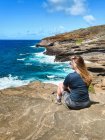Jeune femme aux cheveux longs assis à la plage ensoleillée — Photo de stock