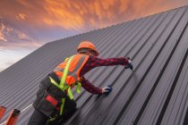 Roofer Trabajador de construcción instalar nuevo techo. Herramientas para techos. Taladro eléctrico utilizado en techos nuevos con chapa metálica. - foto de stock