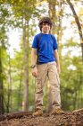 Улыбающийся мальчик, стоящий на стволе дерева в лесу, США — стоковое фото