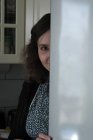 Портрет улыбающейся женщины, прячущейся за дверью на кухне — стоковое фото