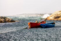 Due barche ancorate nella baia costiera con onde che rotolano su rocce sullo sfondo — Foto stock