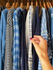Woman hand reaching to blue tops hanging in wardrobe — Stock Photo