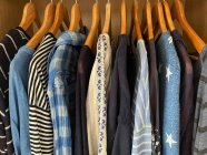 Surtido de tapas azules, blusas, camisas y camisetas colgando en el armario - foto de stock