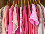 Surtido de tapas de color rosa, blusas, camisetas y camisetas colgando en el armario - foto de stock