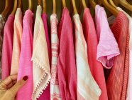 Mano femminile tenuta top rosa con altri top rosa su appendini — Foto stock