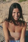 Mulher sorridente sentada na praia com uma flor na boca, Maiorca, Espanha — Fotografia de Stock