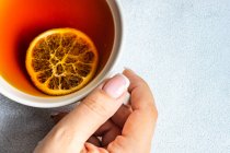 Female hand with cup of tea with dried orange slice inside — Stock Photo