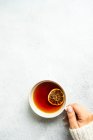 Vista superior de mãos femininas segurando xícara com chá e fatia de laranja seca — Fotografia de Stock
