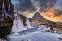 Chute d'eau énorme dans la scène enneigée avec rocher et coucher de soleil ciel — Photo de stock