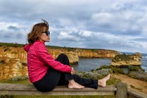 Femme assise sur une clôture regardant la vue, Les douze apôtres, Parc national marin des douze apôtres, Victoria, Australie — Photo de stock