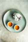Two cups of tea and teapot on plate, top view — Stock Photo
