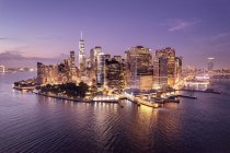 Vista del paseo marítimo y el distrito financiero iluminado por la noche, Manhattan, Nueva York, EE.UU. - foto de stock