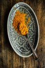 Spoonful of turmeric powder on plate on wooden table — Stock Photo