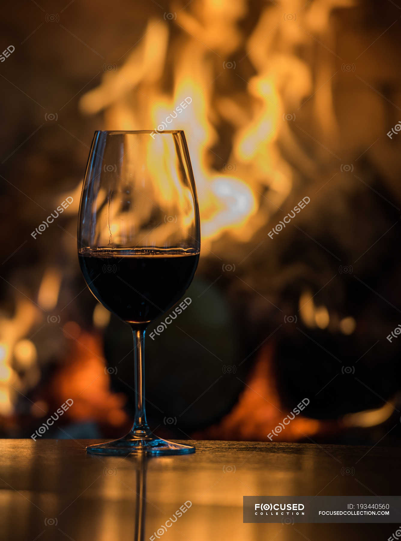 Glass of red wine on a table in front of a fireplace — tasty - Stock | #193440560