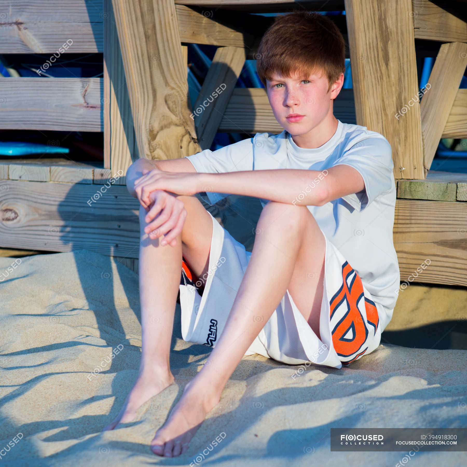 Jovem sentado na praia de areia e encostado ao calçadão Sessão Olhando para a câmera Stock
