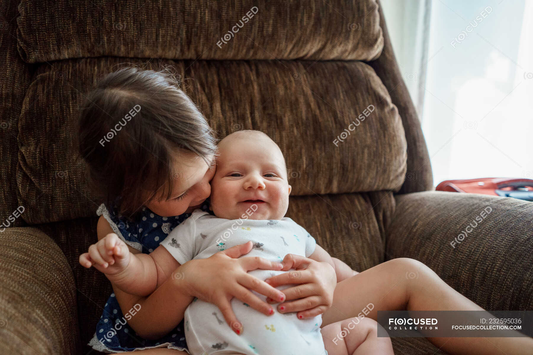 Girl sitting in chair cuddling a baby boy — brother, infant Stock