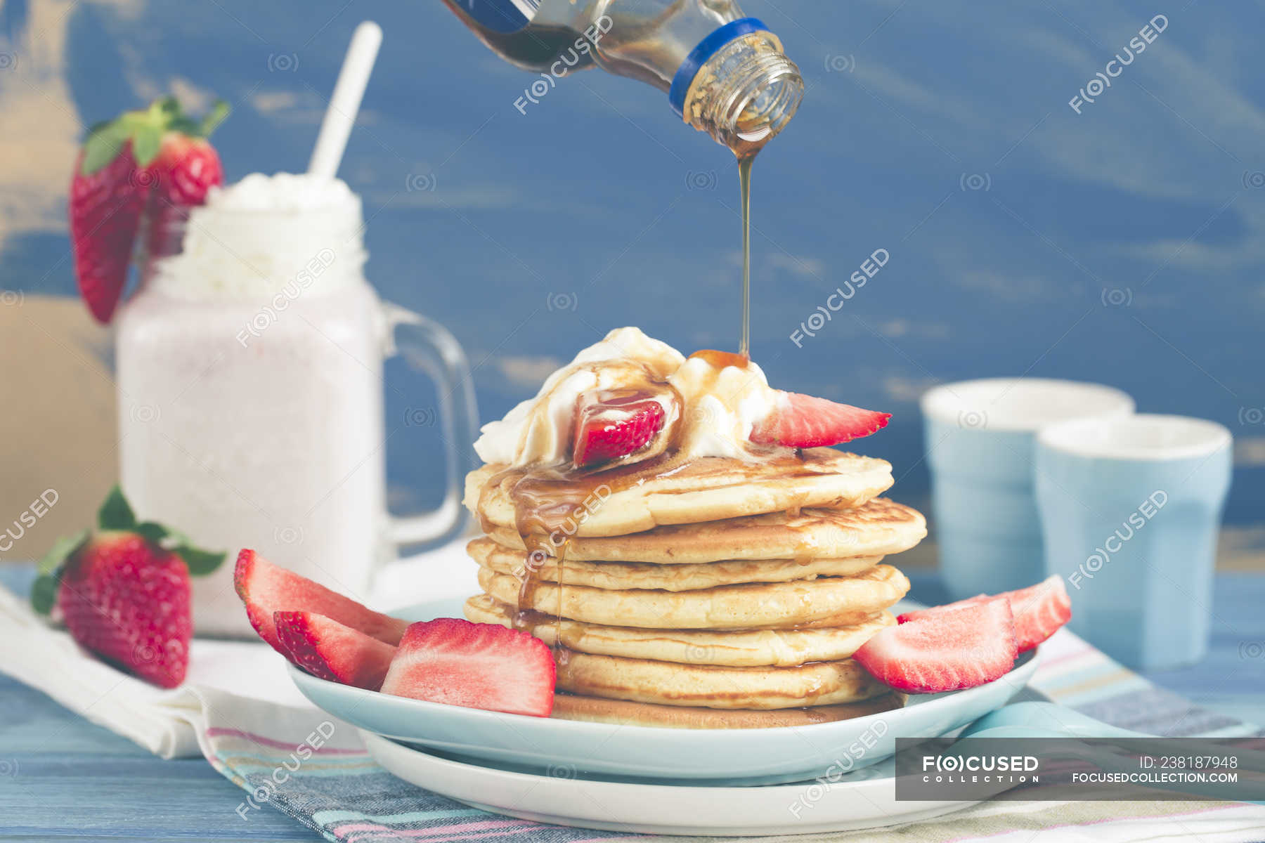 Pouring syrup onto a Stack of pancakes with fresh strawberries — fried