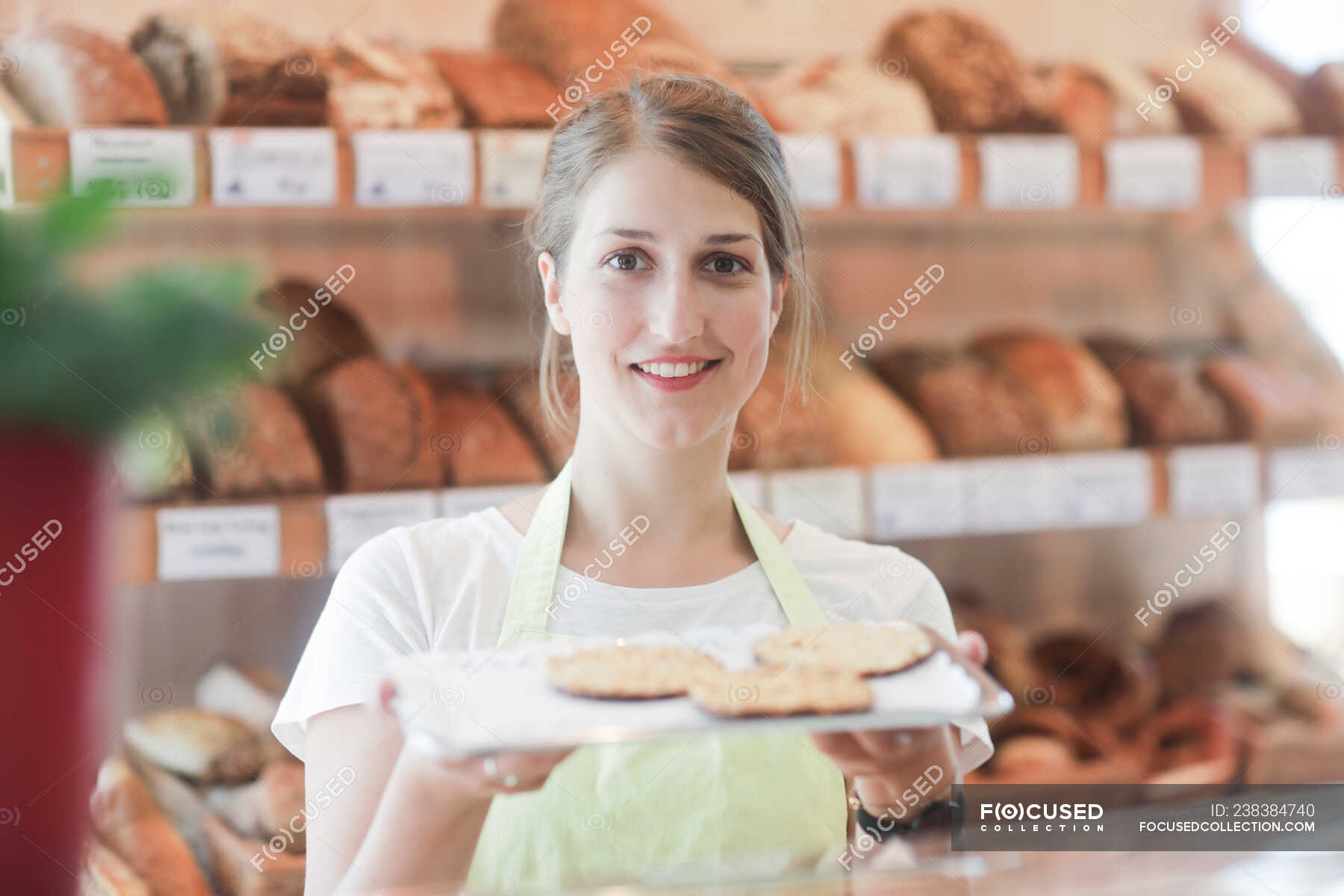 Smiling sales assistant in a bakery holding a tray of samples ...