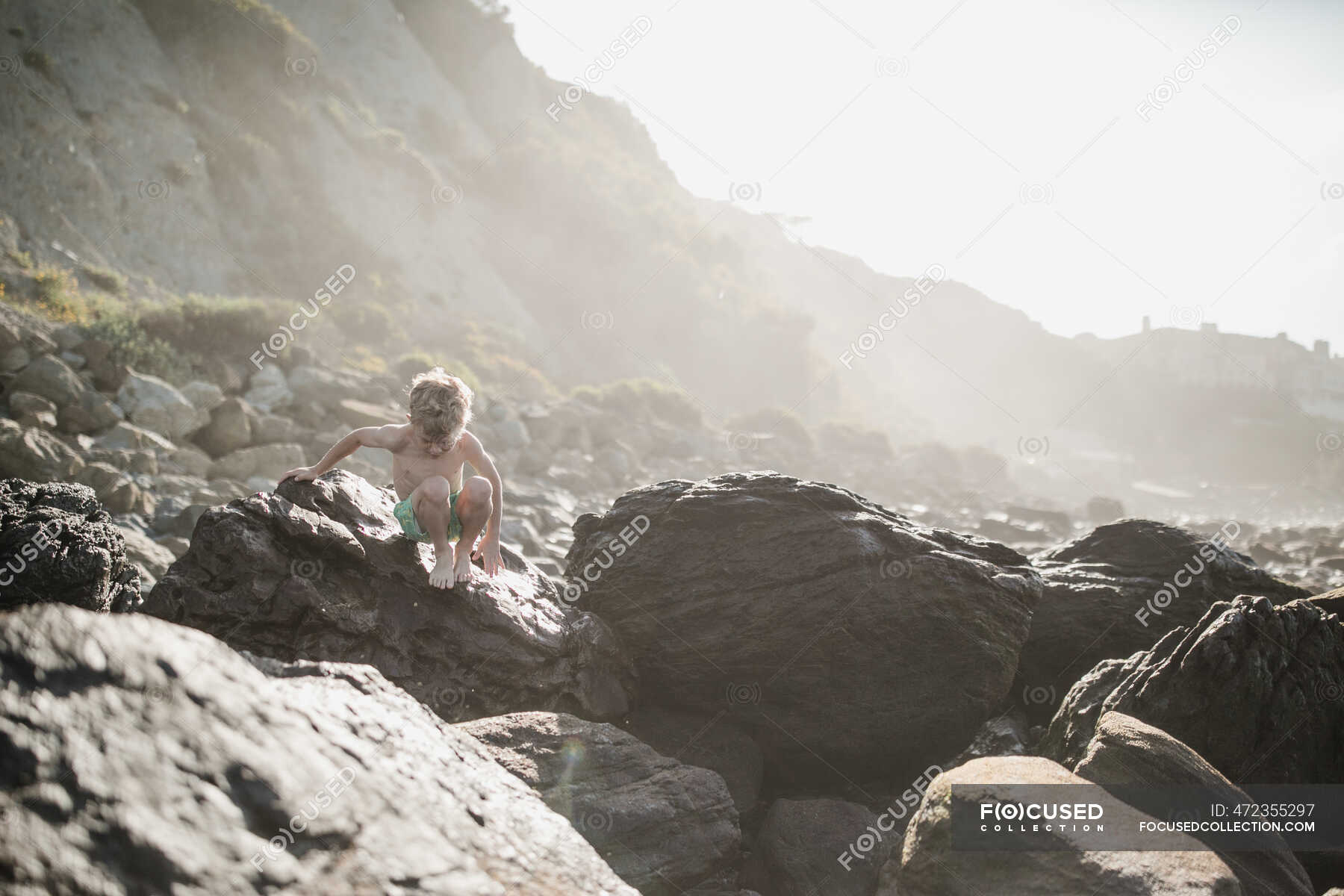 Boy climbing down rocks on beach, Laguna Beach, California, Stati Uniti