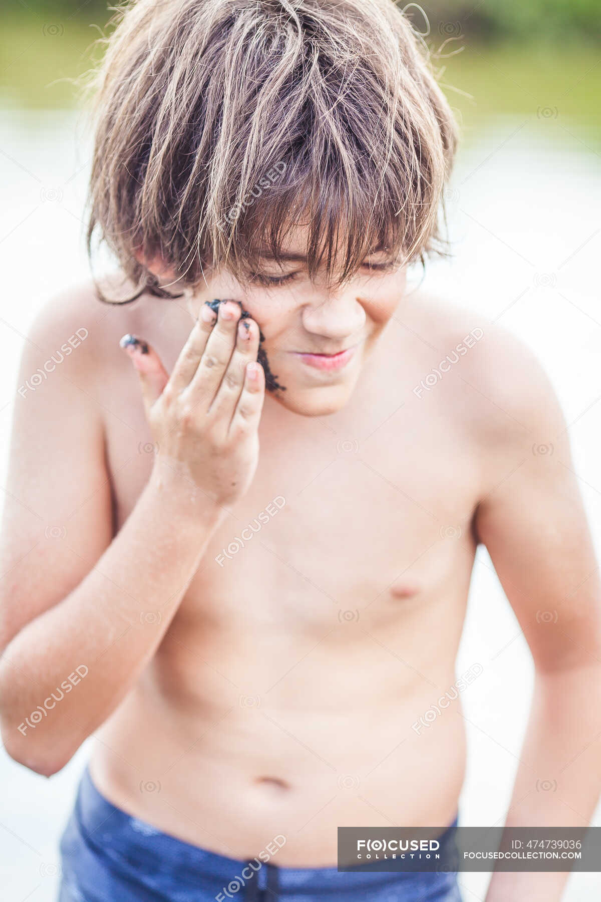 Boy standing in Atanasovsko Lake putting mud on his face ...