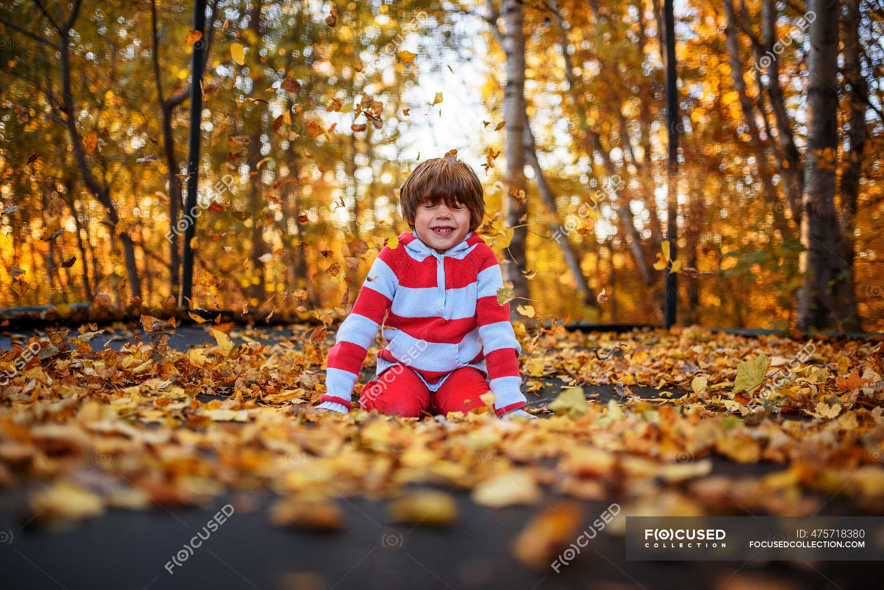 Smiling Boy sitting on a trampoline covered in autumn leaves, United