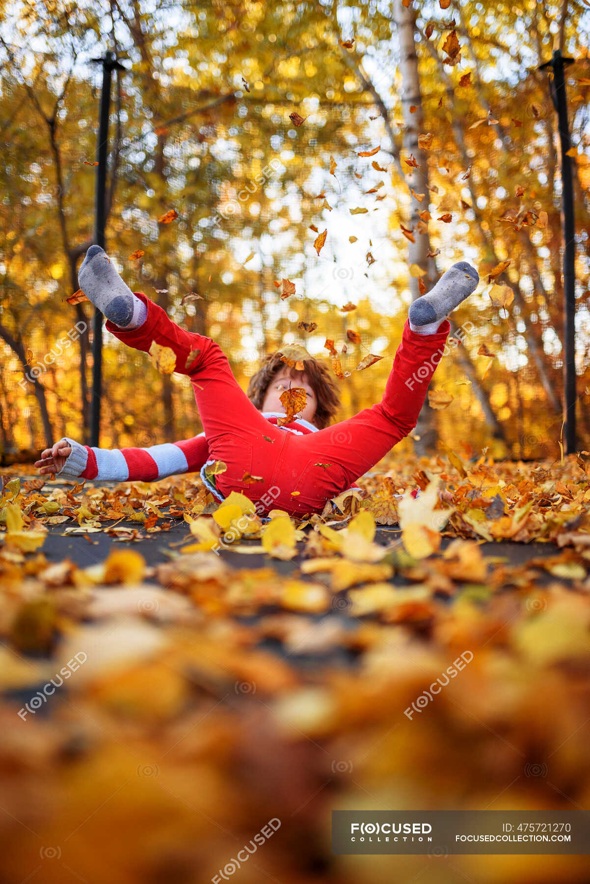 Boy jumping on a trampoline covered in autumn leaves, United States