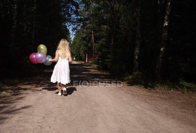 Menina andando com balões na estrada da floresta — Fotografia de Stock