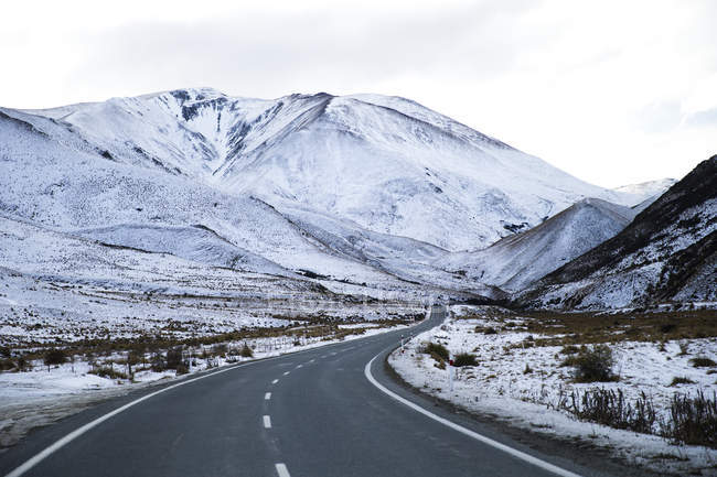 Пустая дорога с заснеженными горами — стоковое фото