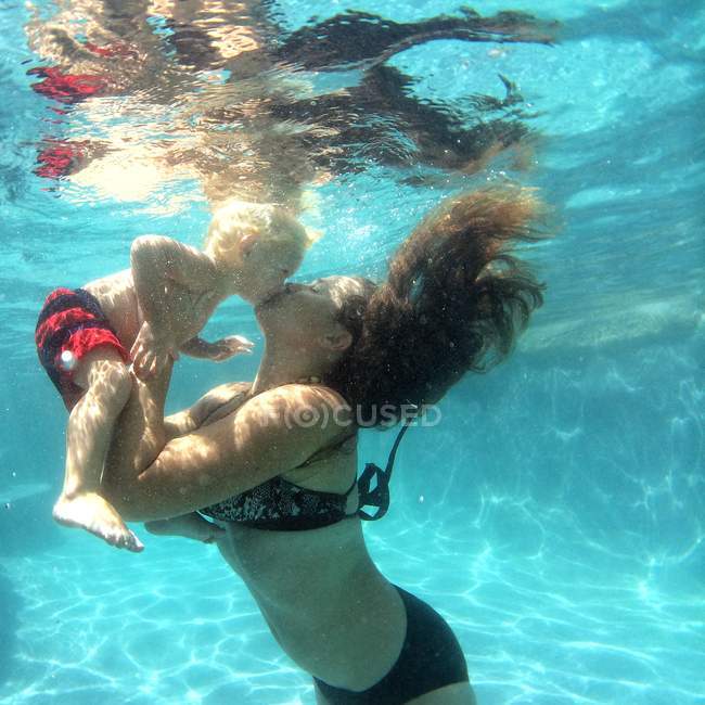 Madre besando bebé bajo el agua - foto de stock