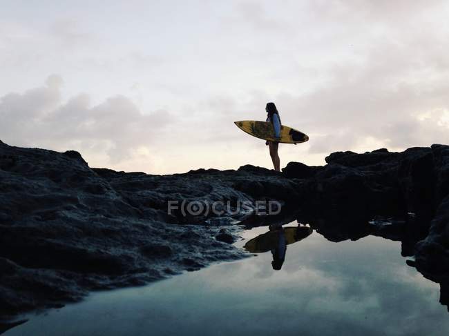 Молодая серфингистка стоит на скале — стоковое фото