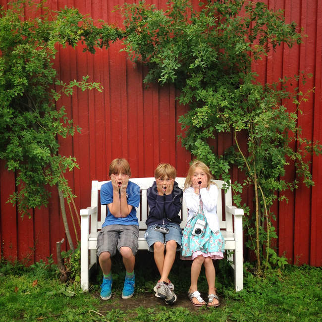 Tres niños sentados en el banco - foto de stock
