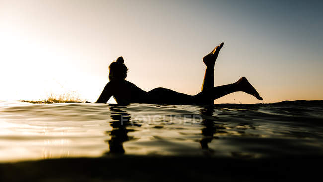 Silueta de mujer sobre tabla de surf - foto de stock
